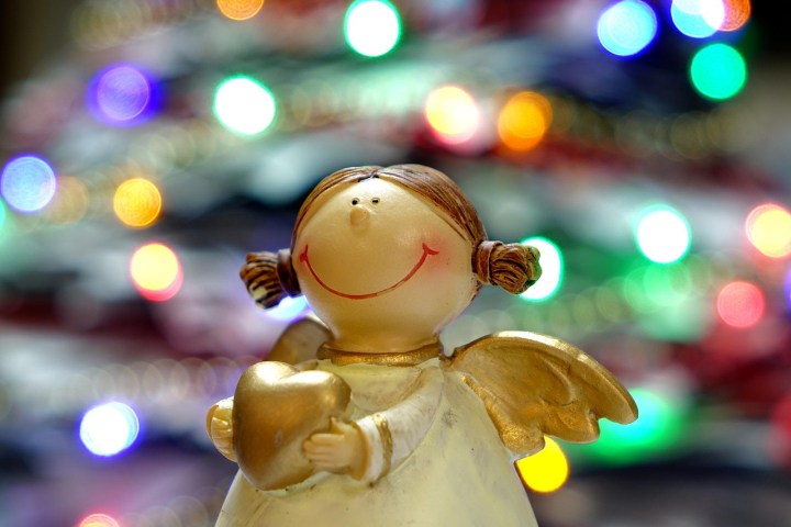 Smiling angel figurine with golden wings and heart against colorful blurred lights.