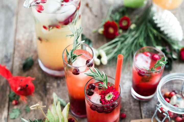 Assorted festive cocktails with rosemary and cranberries on a wooden table.